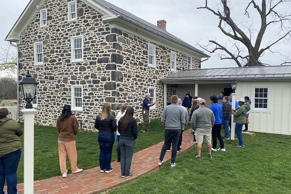 men and women of a corporate team stand on brick walkway near stone house listening to professional leadership development presentations
