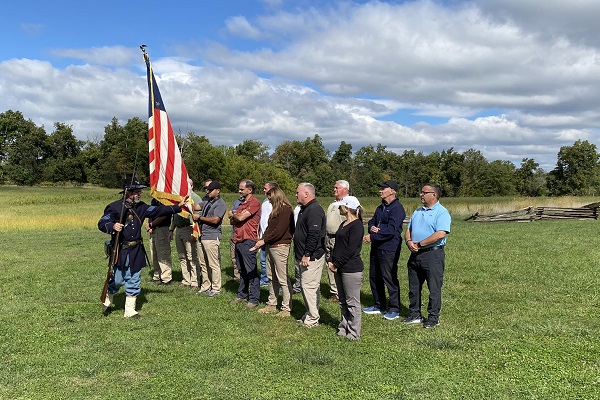 docent in American Civil War period dress with American flag stands before men and women outdoors